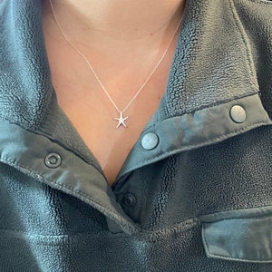 May include: A silver necklace with a small starfish pendant. The necklace is worn by a person wearing a dark green fleece jacket.