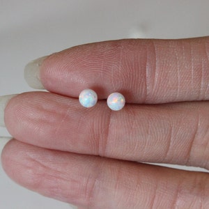 May include: A pair of small, round, white opal stud earrings. The earrings are set in silver.