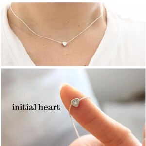 K&ouml;nnte beinhalten: Eine silberne Halskette mit einem kleinen Herz-Anh&auml;nger. Das Herz hat eine einzelne Initial im Inneren graviert. Der Text "initial heart" ist unterhalb der Halskette sichtbar.