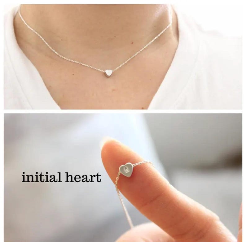 K&ouml;nnte beinhalten: Eine silberne Halskette mit einem kleinen Herz-Anh&auml;nger. Das Herz hat eine einzelne Initial im Inneren graviert. Der Text "initial heart" ist unterhalb der Halskette sichtbar.
