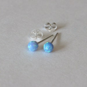 May include: A pair of silver stud earrings with blue opal stones.
