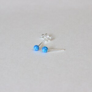May include: A pair of silver stud earrings with small, round blue opal stones.