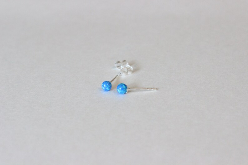 May include: A pair of silver stud earrings with small, round blue opal stones.