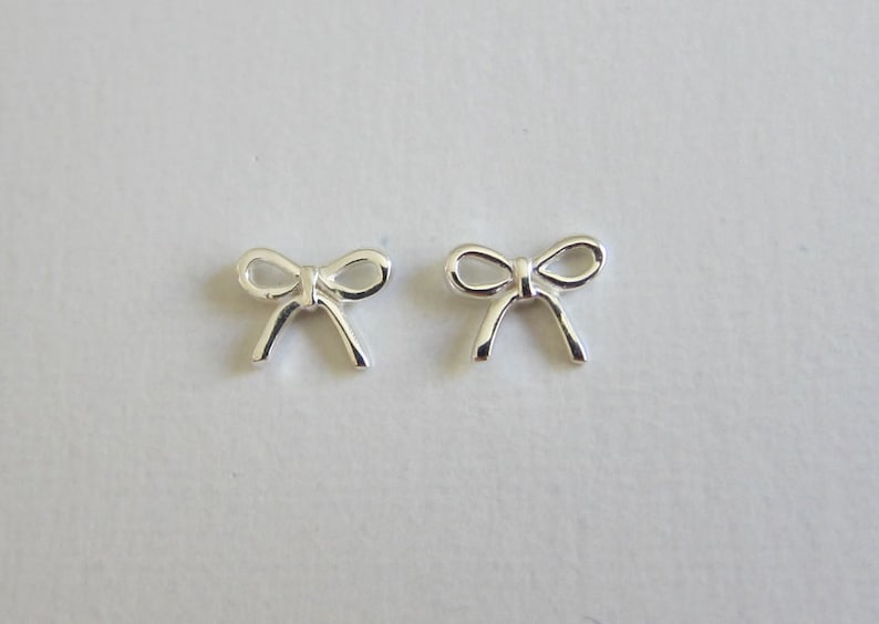 May include: A pair of silver bow-shaped stud earrings.