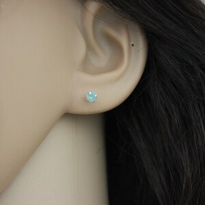 May include: A close-up of a person's ear with a small, light blue gemstone stud earring.