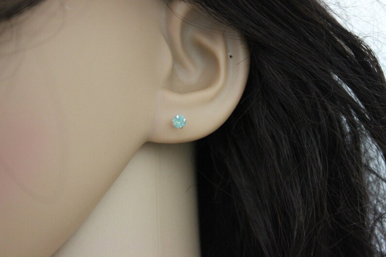 May include: A close-up of a person's ear with a small, light blue gemstone stud earring.