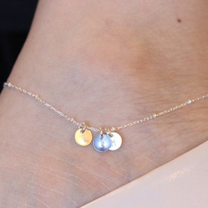 Könnte beinhalten: Ein silbernes Fußkettchen mit drei kleinen runden Anhängern. Die Anhänger sind silber, gold und blau.