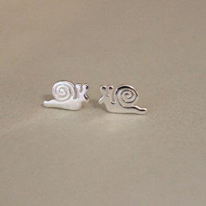 May include: A pair of silver snail stud earrings. The snails are facing the same direction and have a simple, minimalist design.