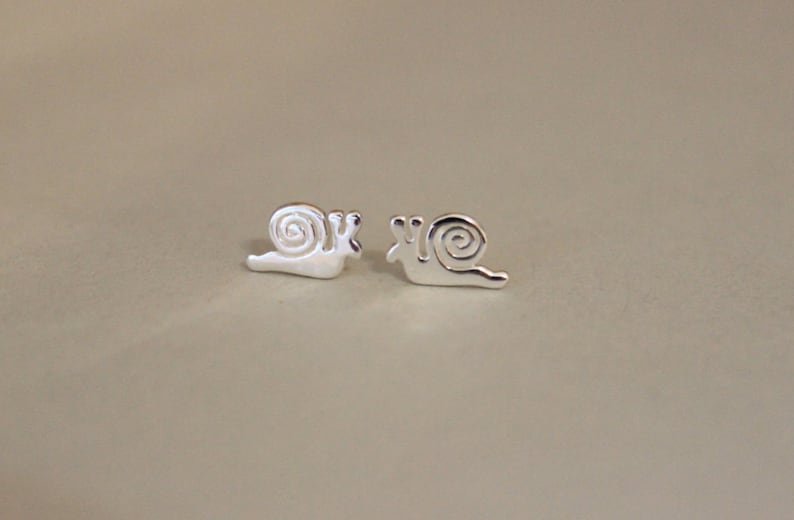May include: A pair of silver snail stud earrings. The snails are facing the same direction and have a simple, minimalist design.