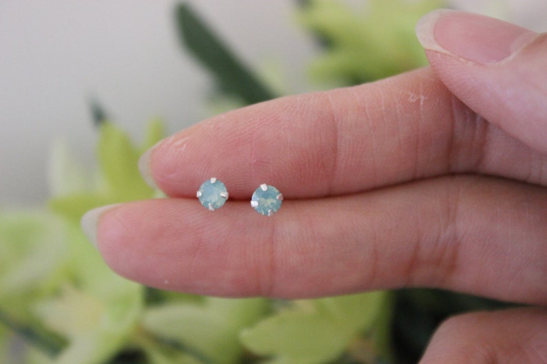 May include: A pair of silver stud earrings with small, round, light blue opal stones.