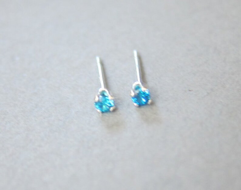 Puede incluir: Un par de pendientes de bot&oacute;n de plata con peque&ntilde;as piedras azules.
