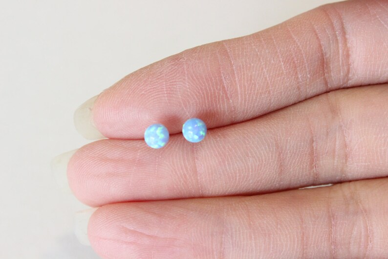 May include: A pair of small, round, blue opal stud earrings.