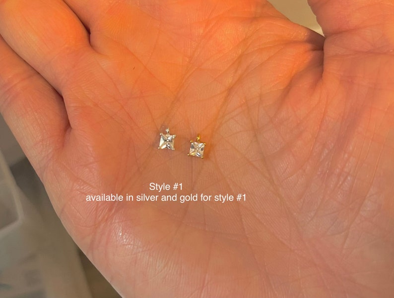 May include: Two small square-cut gemstone pendants, one silver and one gold, are displayed. The image includes text that reads "Style #1 available in silver and gold for style #1."
