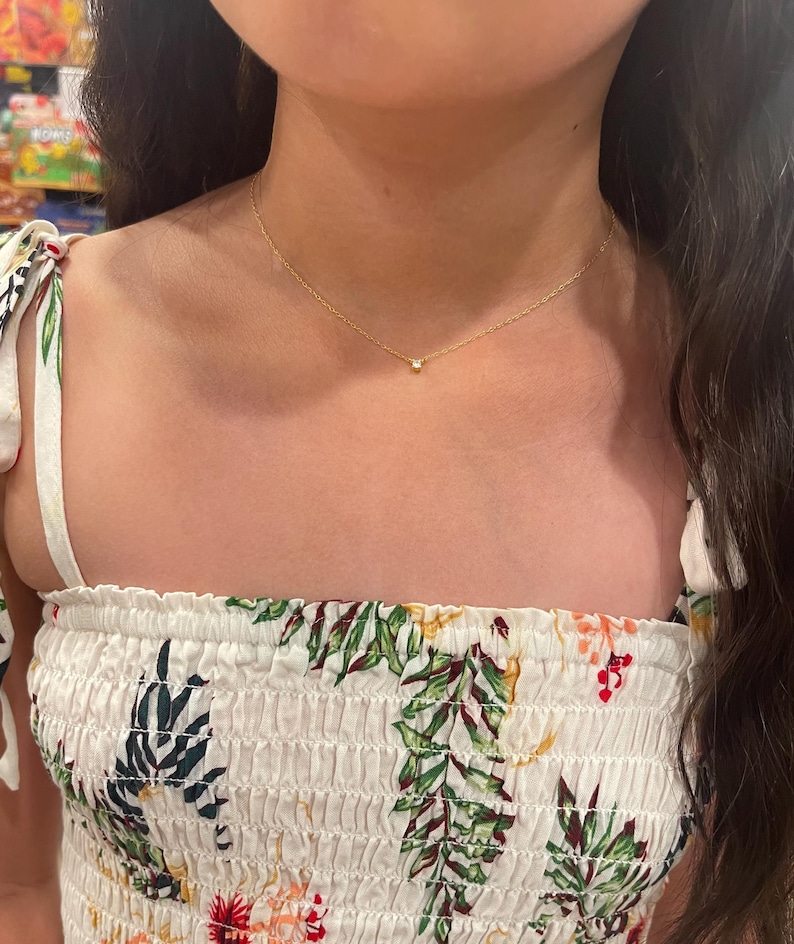 May include: A delicate gold chain necklace with a small, clear gemstone pendant.