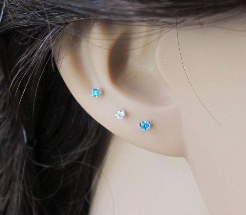 Puede incluir: Tres peque&ntilde;os pendientes de bot&oacute;n con piedras preciosas transparentes y azules. Los pendientes se llevan en el l&oacute;bulo de la oreja y en el piercing del h&eacute;lix.