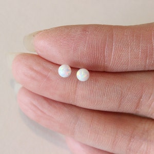 May include: A pair of white opal stud earrings. The earrings are small and round, and they have a subtle iridescent shimmer.