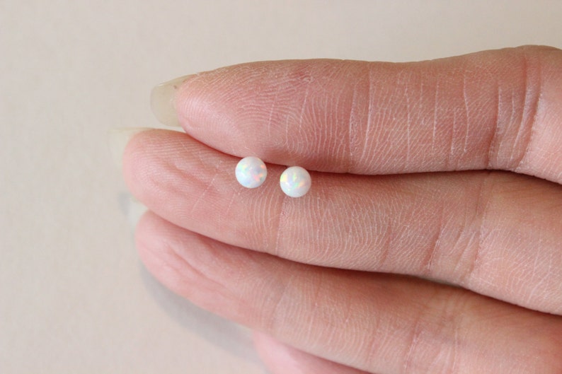 May include: A pair of white opal stud earrings. The earrings are small and round, and they have a subtle iridescent shimmer.