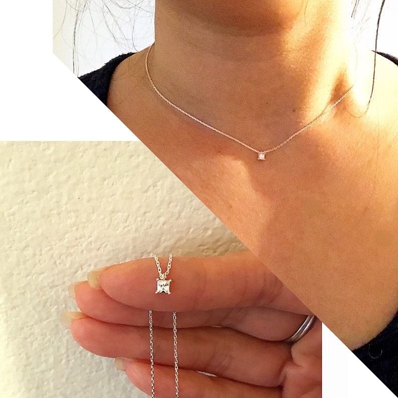 May include: Delicate silver necklace featuring a small, square-cut gemstone pendant. The necklace is shown on a person's neck and hand, highlighting the pendant's subtle sparkle. The chain is thin and elegant, suitable for everyday wear or special occasions.