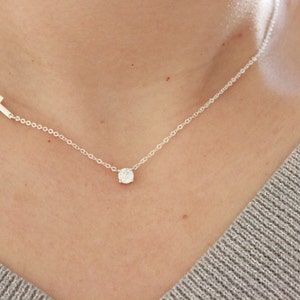 May include: A silver chain necklace with a small, round, clear gemstone pendant and a small silver cross charm.