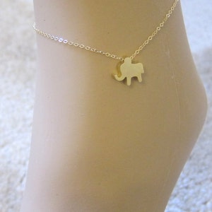 Puede incluir: Un tobillo de oro con un pequeño encanto de elefante. El tobillo es delicado y fino.