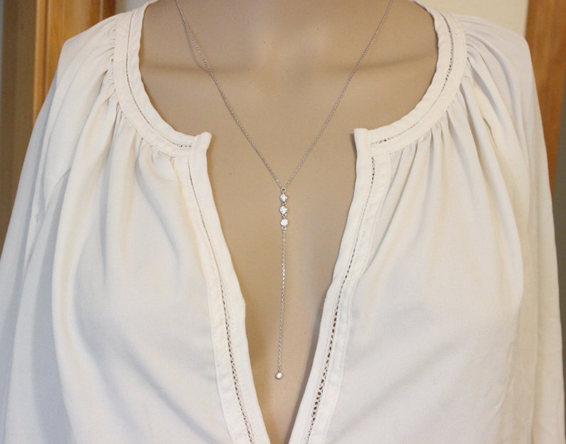 May include: A silver chain necklace with three small round stones and a larger stone at the bottom.