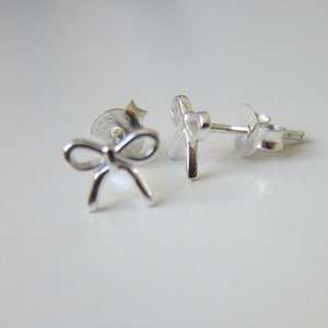 May include: A pair of silver bow-shaped stud earrings. The earrings are small and delicate, and they would make a great gift for a special occasion.