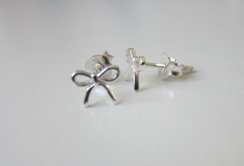 May include: A pair of silver bow-shaped stud earrings. The earrings are small and delicate, and they would make a great gift for a special occasion.