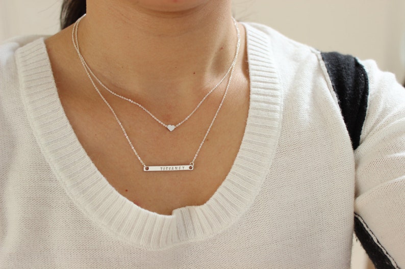 K&ouml;nnte beinhalten: Eine silberne Halskette mit einem kleinen Herz-Anh&auml;nger und einem l&auml;ngeren Barren-Anh&auml;nger mit der Gravur "perfekt".