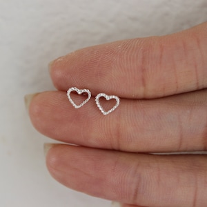 May include: A pair of silver heart-shaped stud earrings with a beaded edge.
