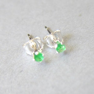 May include: A pair of silver stud earrings with small green gemstones.