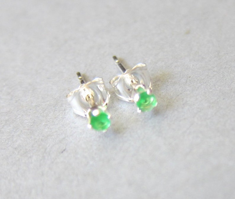 May include: A pair of silver stud earrings with small green gemstones.