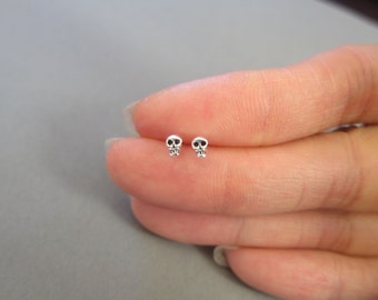 May include: A pair of silver skull stud earrings. The skulls are small and detailed, with black eyes.