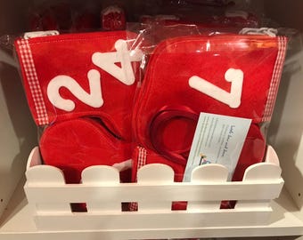 May include: Red felt Christmas stocking ornaments with white numbers 24 and 7. The stockings are in a white picket fence-style basket.
