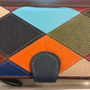 May include: A rectangular wallet featuring a multi-colored diamond patchwork pattern in shades of orange, light blue, olive green, dark blue, cream, and maroon. The wallet has a textured leather-like surface and a dark blue snap-button closure tab.
