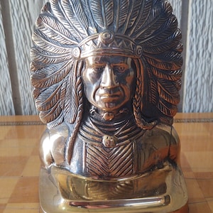 Puede incluir: Busto de bronce de un jefe nativo americano, con un tocado detallado con detalles de plumas. La escultura tiene un acabado pulido y est&aacute; sobre una base rectangular. Es un art&iacute;culo decorativo.