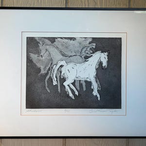 May include: A framed black and white etching print titled Shadows, numbered 4/20, and signed by Carol Krier Taylor. The artwork depicts a white horse in the foreground with a ghostly, translucent horse silhouette behind it against a dark background.