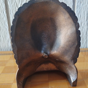 Puede incluir: Cenicero decorativo de color bronce con borde festoneado. El cenicero tiene forma de cuenco poco profundo y est&aacute; sostenido por tres patas. La superficie tiene un aspecto ligeramente texturizado.