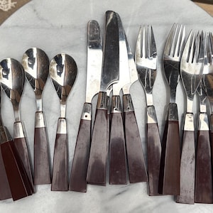 May include: A set of stainless steel flatware featuring dark brown plastic handles. The collection includes four spoons, three knives with serrated blades, and four forks. Each piece has a silver metal top and a solid brown handle with a metal ferrule.
