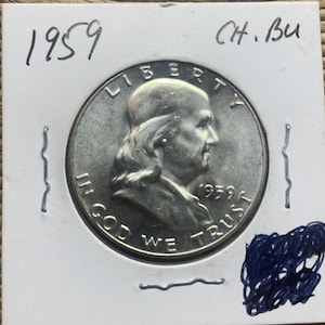 May include: A silver 1959 Franklin half dollar coin, featuring a profile of Benjamin Franklin. The coin is in a protective holder, with handwritten text reading "1959" and "Ch. Bu". The coin's inscriptions include "Liberty" and "In God We Trust".