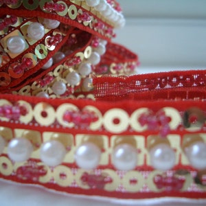 May include: Red and gold trim with white pearl beads. The trim has a red velvet backing and is decorated with sequins and small pink beads.