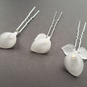 Puede incluir: Tres horquillas de pelo plateadas con abalorios de vidrio esmerilado en forma de pera y diamantes de imitación transparentes. Cada abalorio tiene un diseño de hoja.