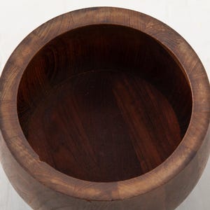 May include: A handcrafted, dark brown wooden bowl with a wide, rounded rim. The bowl's interior is a deep, rich brown, and the wood grain is visible throughout. The bowl is likely used for serving or display.