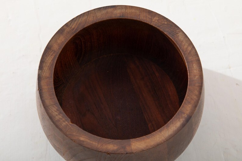 May include: A handcrafted, dark brown wooden bowl with a wide, rounded rim. The bowl's interior is a deep, rich brown, and the wood grain is visible throughout. The bowl is likely used for serving or display.