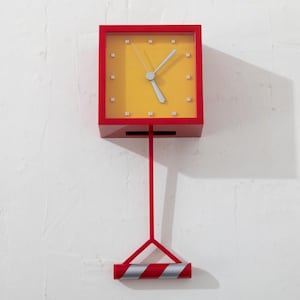 May include: A red square wall clock with a yellow face and silver hands. The clock is suspended by a red rod and a red and silver striped base. The clock's dimensions are approximately 10 inches high.