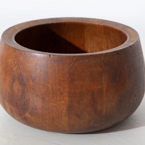 May include: A round, wooden bowl with a dark brown finish. The bowl has a wide opening and a rounded base. The wood grain is visible, adding texture to the piece. This decorative bowl is suitable for various uses.