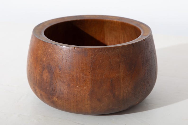 May include: A round, wooden bowl with a dark brown finish. The bowl has a wide opening and a rounded base. The wood grain is visible, adding texture to the piece. This decorative bowl is suitable for various uses.