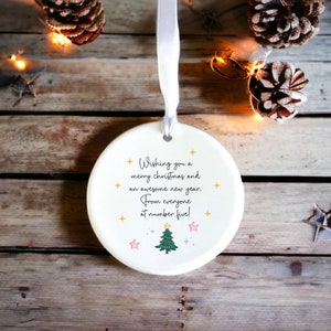May include: White ceramic Christmas bauble with a green Christmas tree and gold stars. The bauble has the text "Wishing you a merry christmas and an awesome new year. From everyone at number five!"