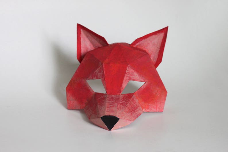 May include: A red paper mask shaped like a fox head. The mask has a black nose and eye holes.