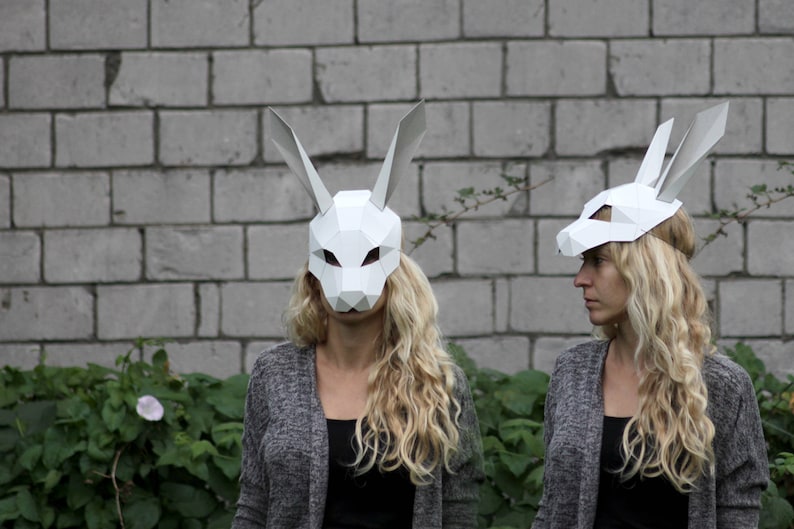 Puede incluir: Dos personas con m&aacute;scaras de conejo de papel mach&eacute; blanco. Las m&aacute;scaras tienen orejas grandes y son de forma geom&eacute;trica. Las personas llevan su&eacute;teres grises y tienen el pelo largo y rubio.