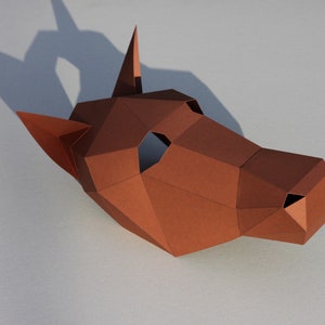 May include: A brown paper mask shaped like a dog's head. The mask has a hole for the eyes and a small hole for the nose.